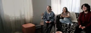 Three teenagers hanging out together in a living room, playing video games